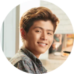 A circular headshot of a young man with brown, wavy hair smiling at the camera.