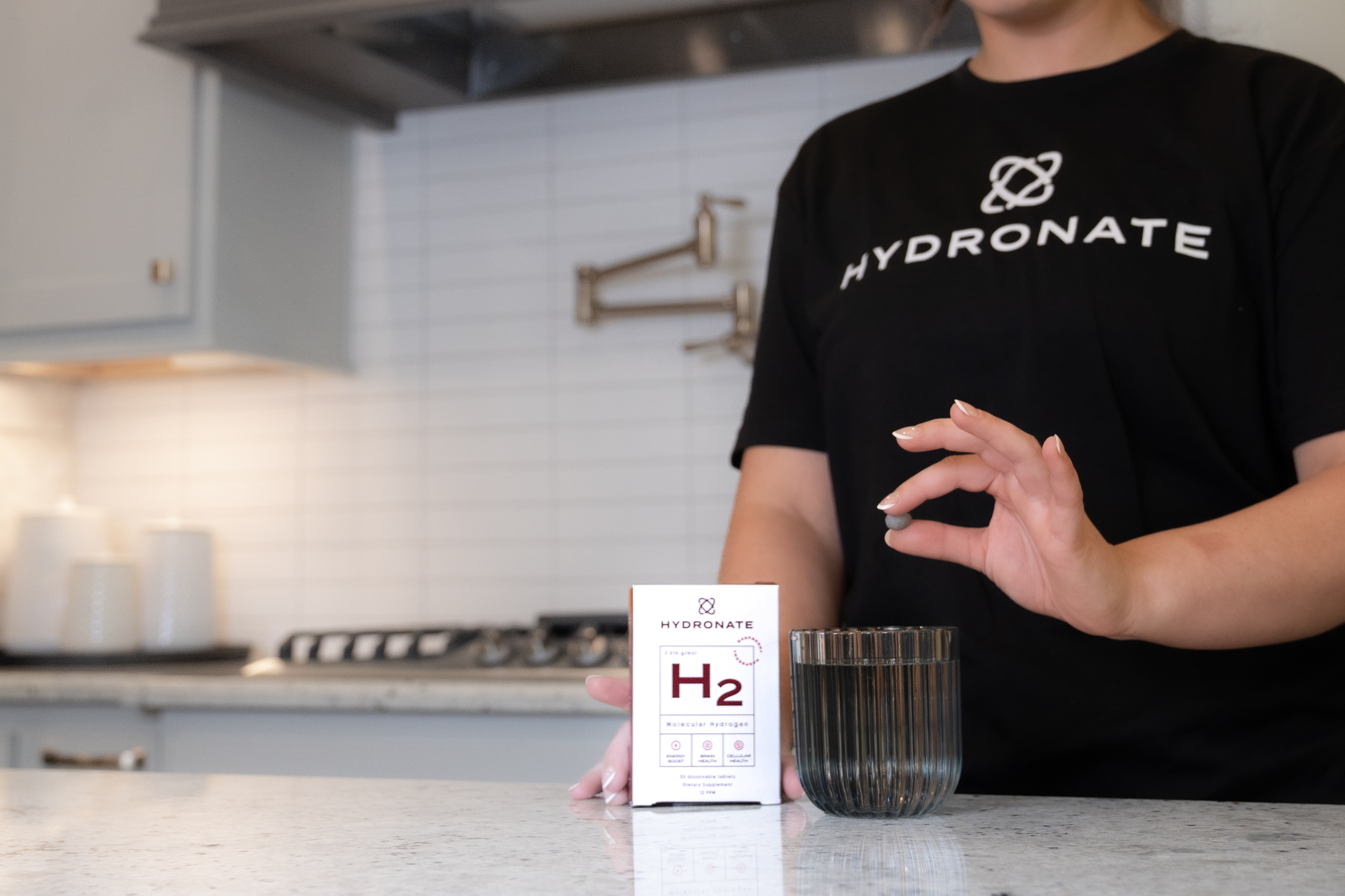 Person holding a glass next to a Hydronate H2 product box.
