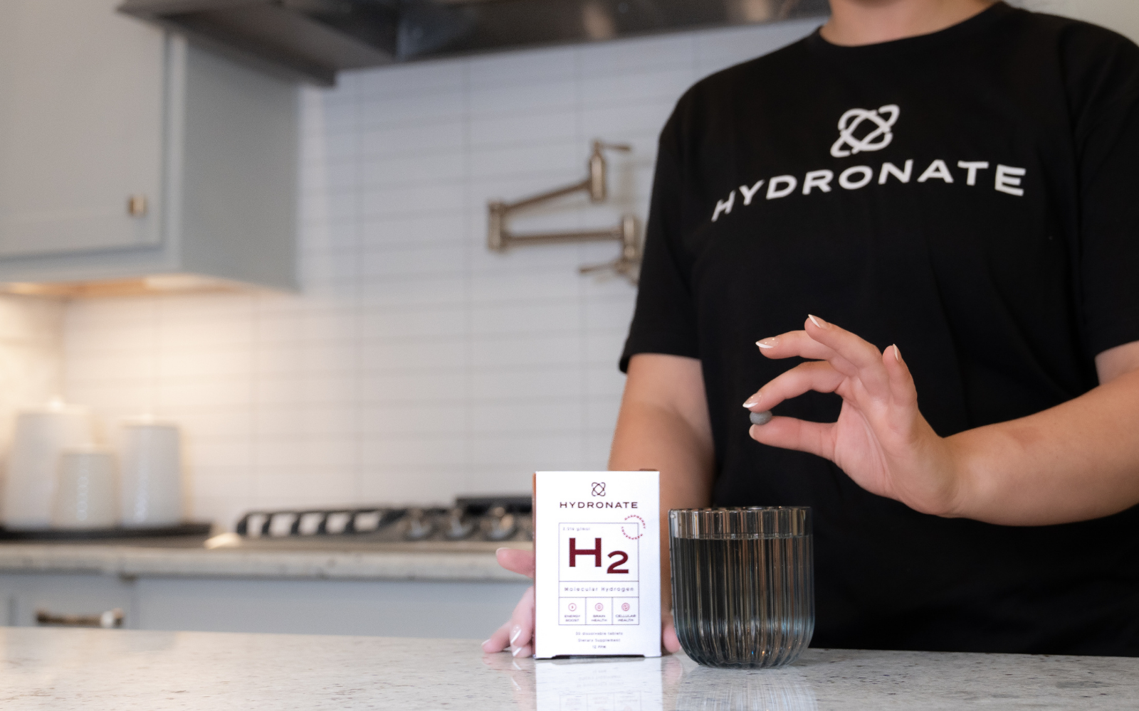 Person holding a tablet above a glass, next to a Hydronate product box.