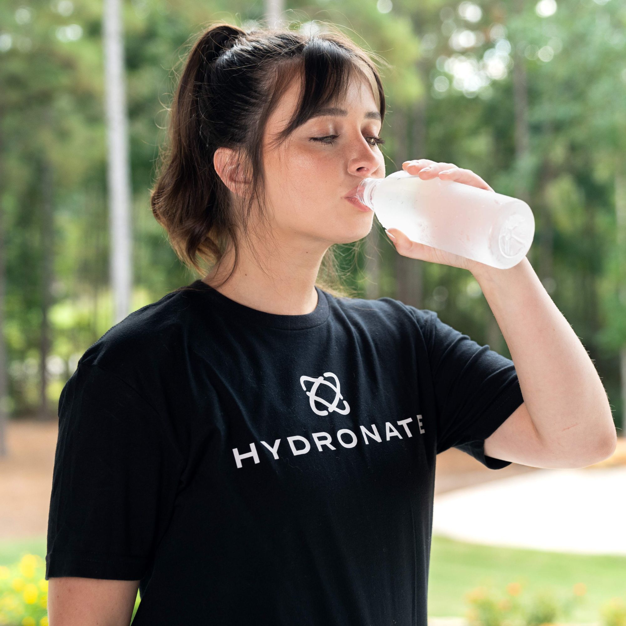 Person in a black shirt drinking from a bottle outdoors.