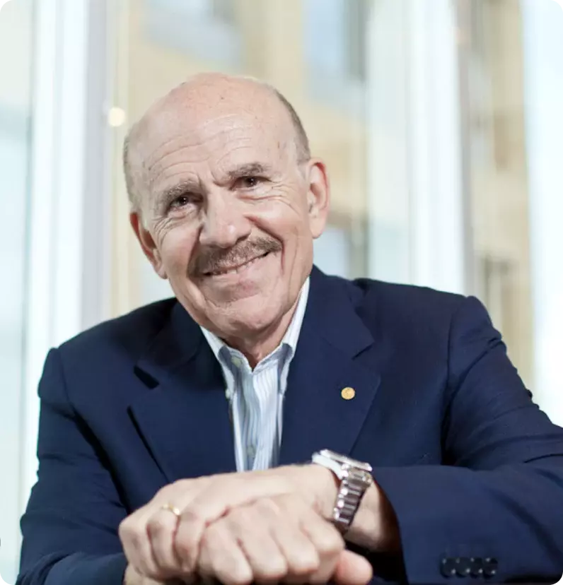 Smiling man in a suit, resting his arms on a table.