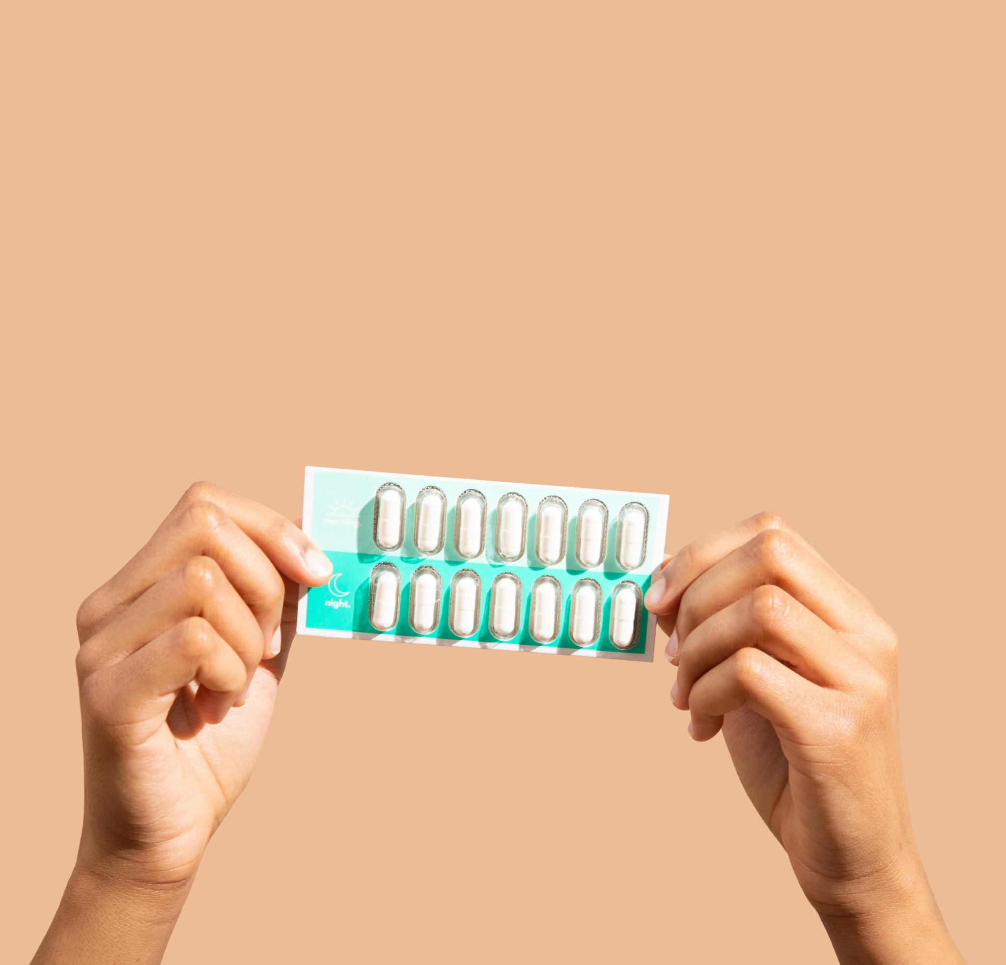 Hands holding a blister pack of capsules against a beige background.