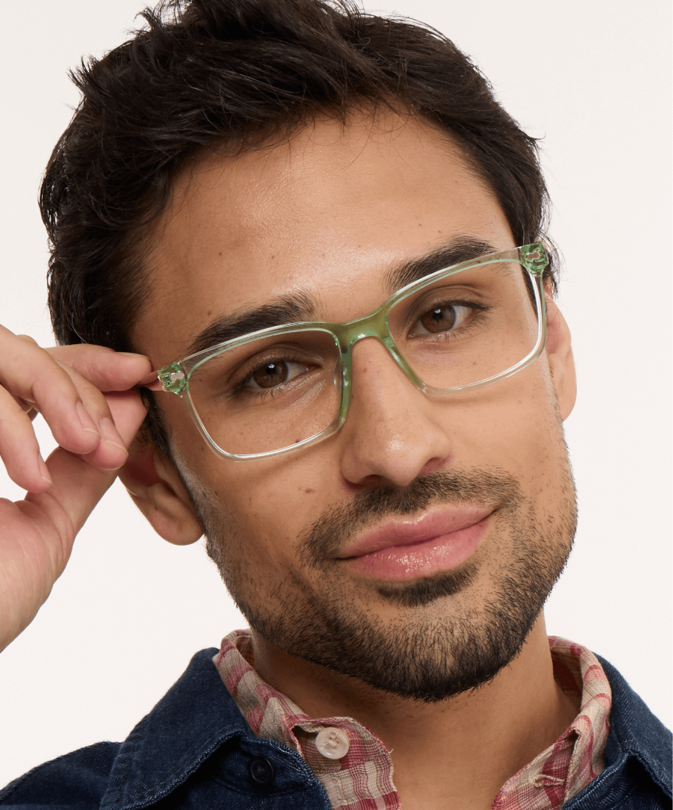 Person wearing green glasses and a plaid shirt, touching the glasses.