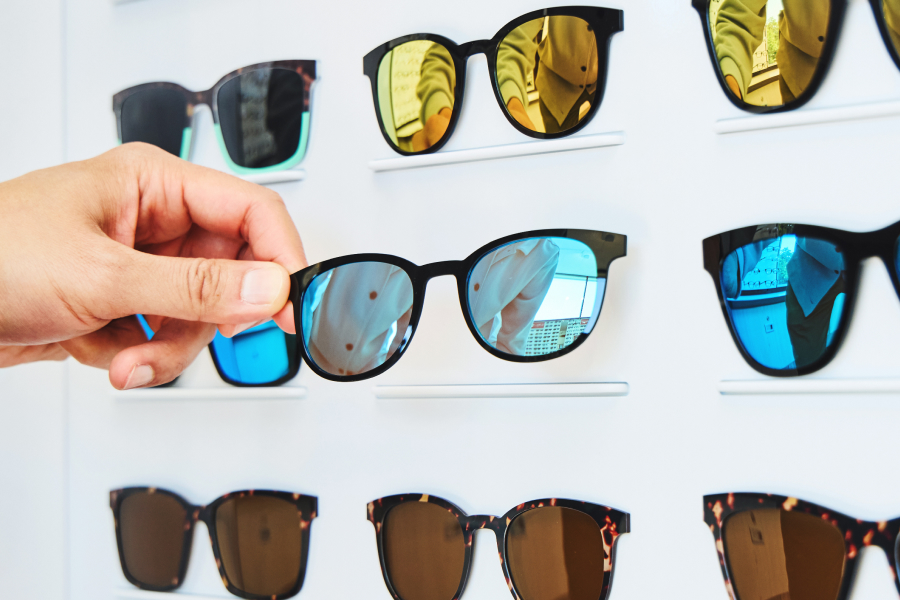 Hand selecting sunglasses from a display with various styles.