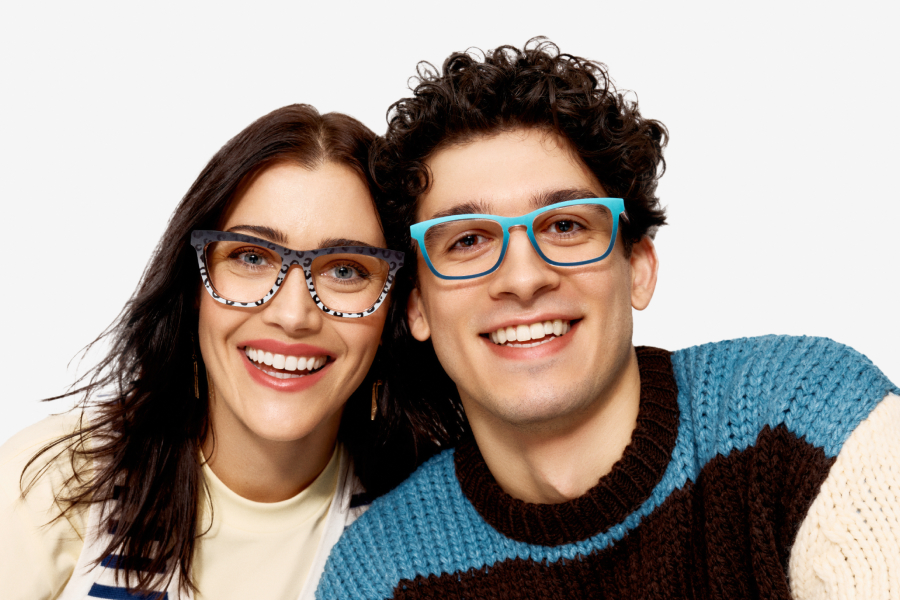 Two people smiling, wearing colorful glasses against a plain background.