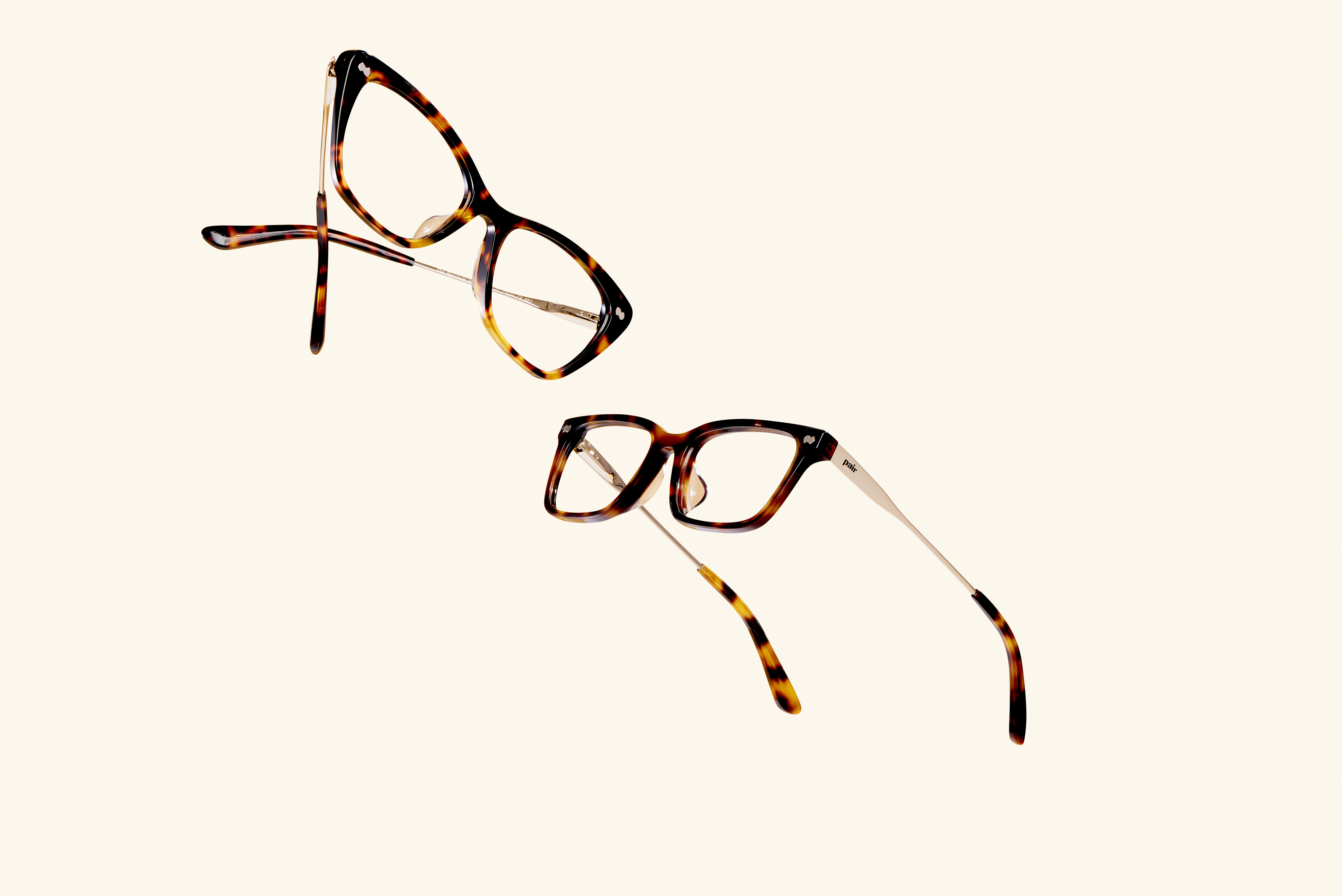Two pairs of tortoiseshell eyeglasses on a plain background.