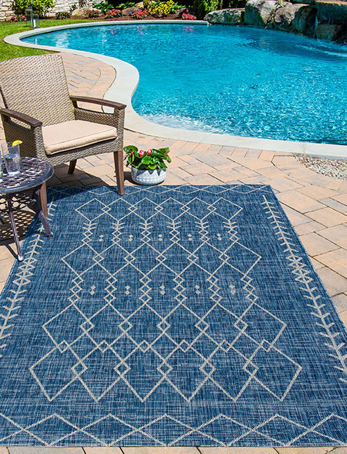 Outdoor patio with a blue patterned rug, chair, table, and pool.