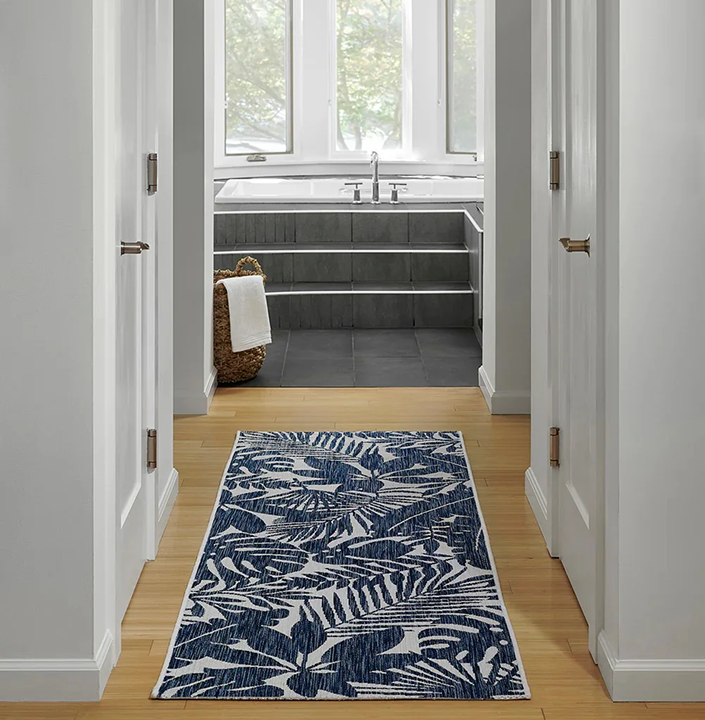 Hallway with a blue patterned rug leading to a bathroom with a bathtub.