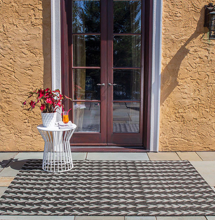 Outdoor patio with a patterned rug, table, plant, and drink.