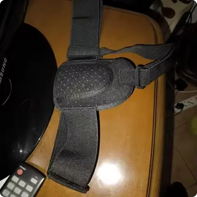 A black head strap with adjustable bands sits on a wooden table next to a remote control.
