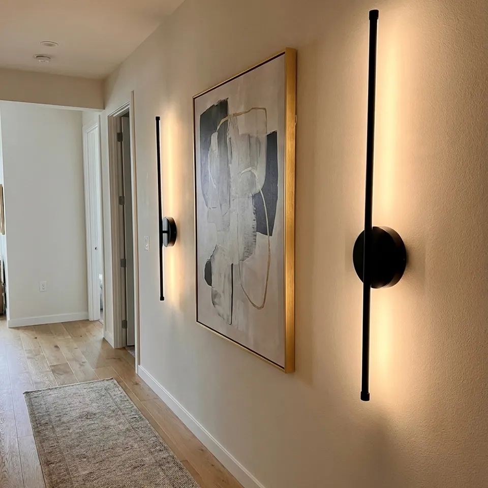 A hallway with hardwood floors, modern black wall sconces, and a large piece of abstract art.