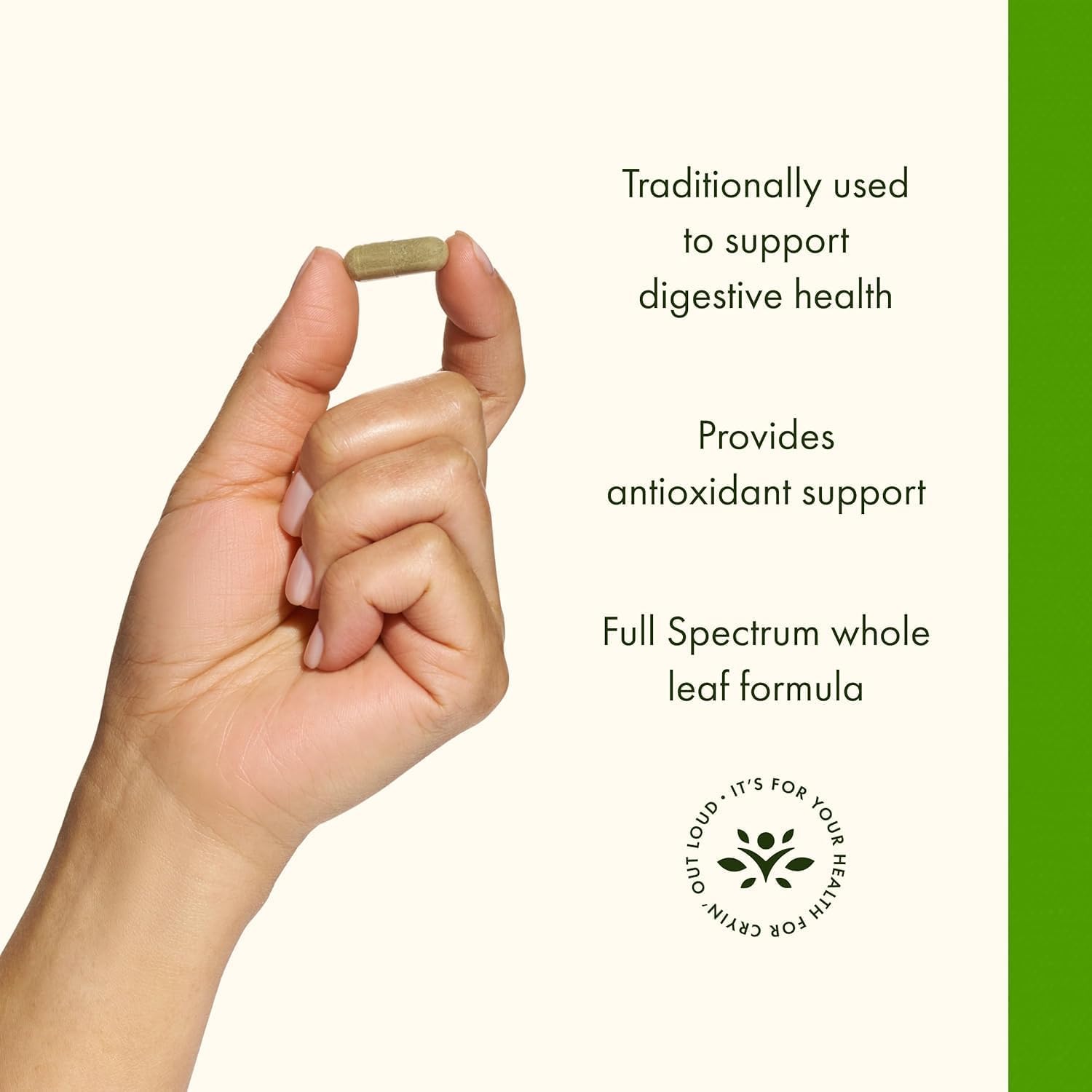 A hand holds a single green supplement capsule between the thumb and forefinger against an off-white background.