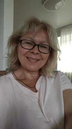 Person with glasses smiling indoors with soft lighting.