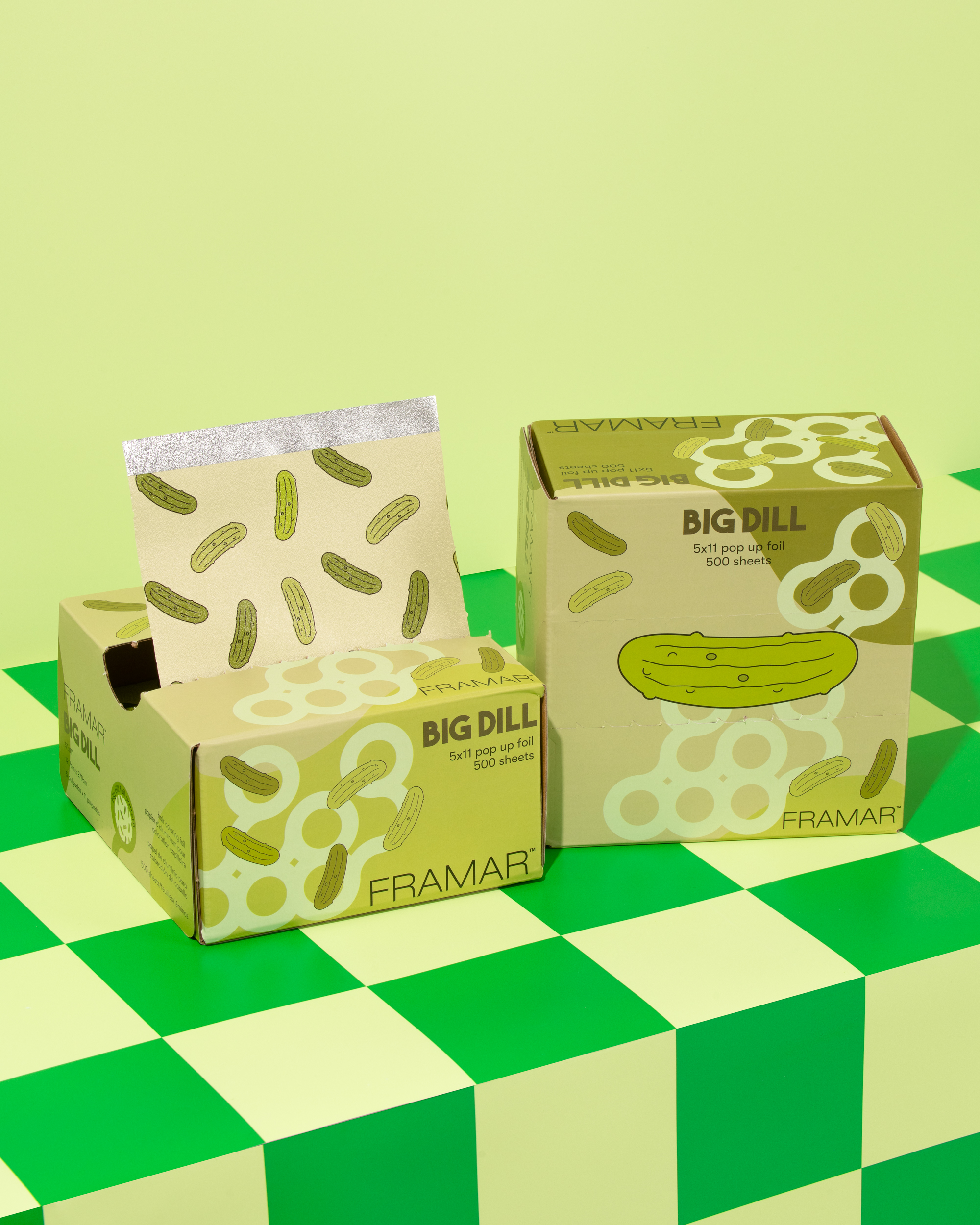 Two boxes of foil sheets with pickle designs on a checkered surface.
