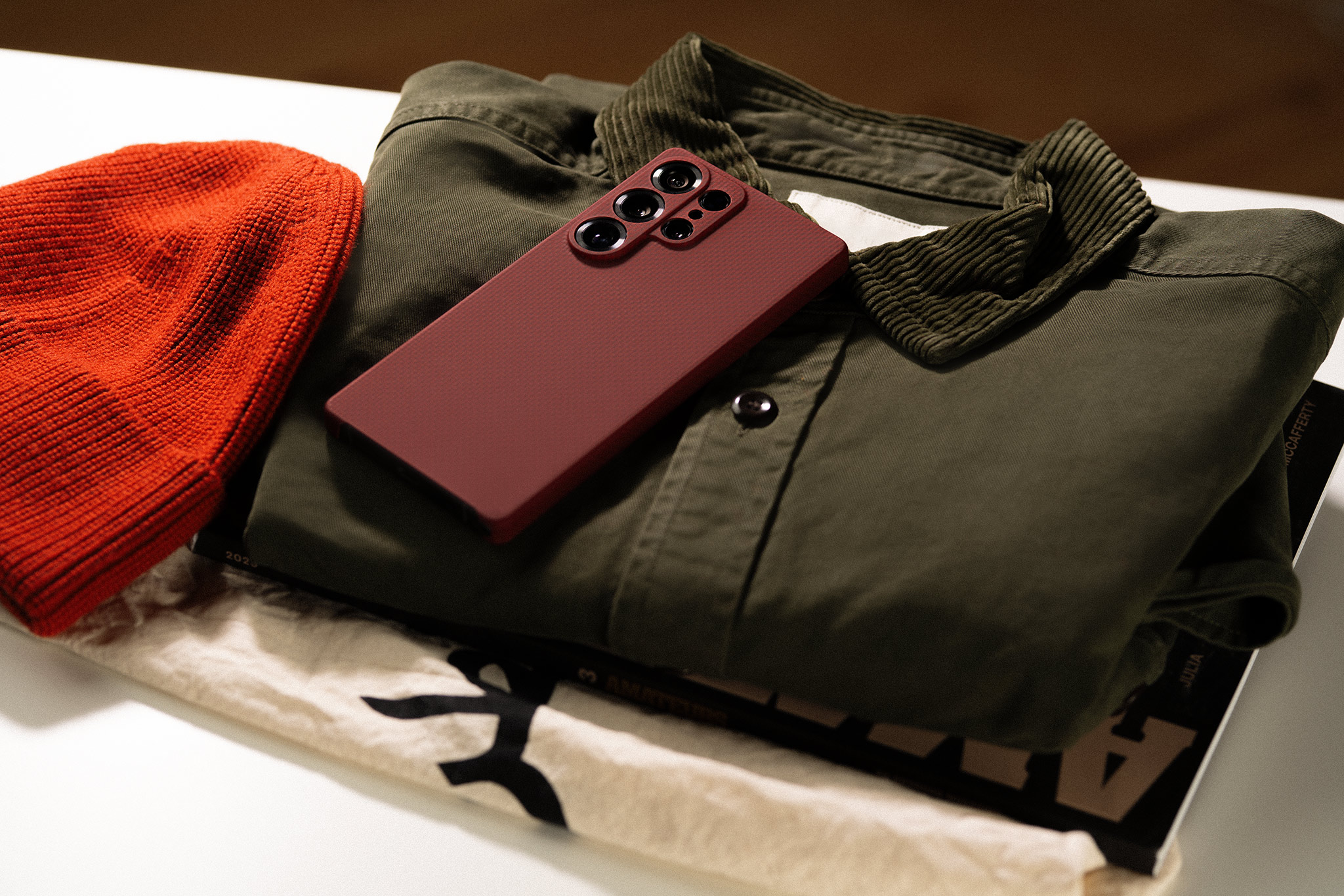 Red phone on folded green shirt next to an orange beanie.