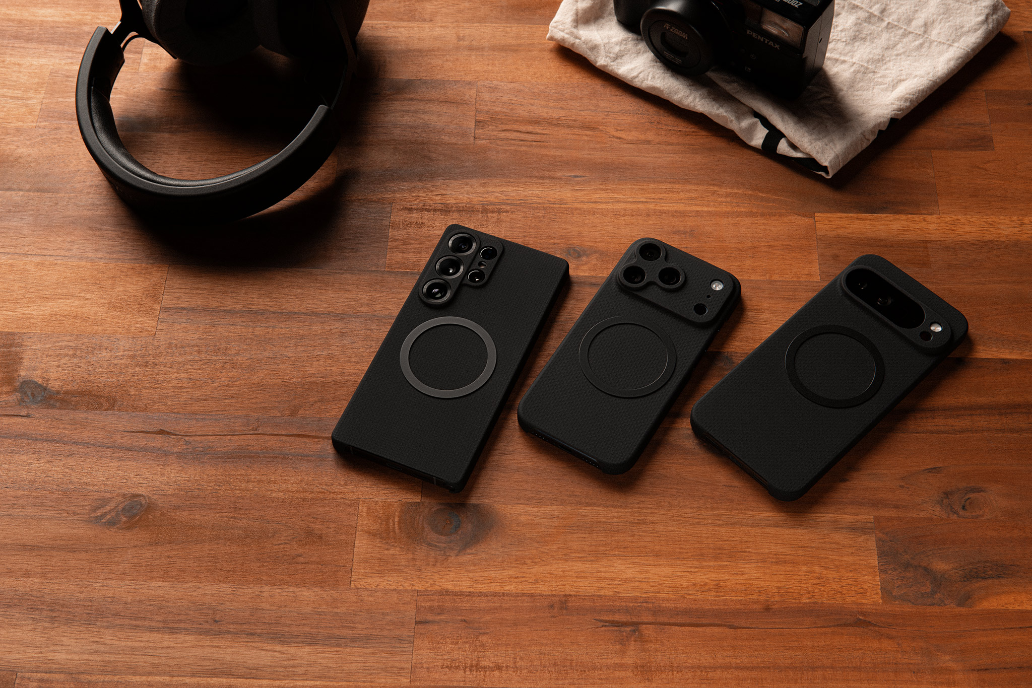Three smartphones with black cases on a wooden table.
