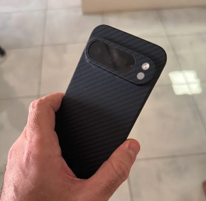 Hand holding a smartphone with a carbon fiber case.