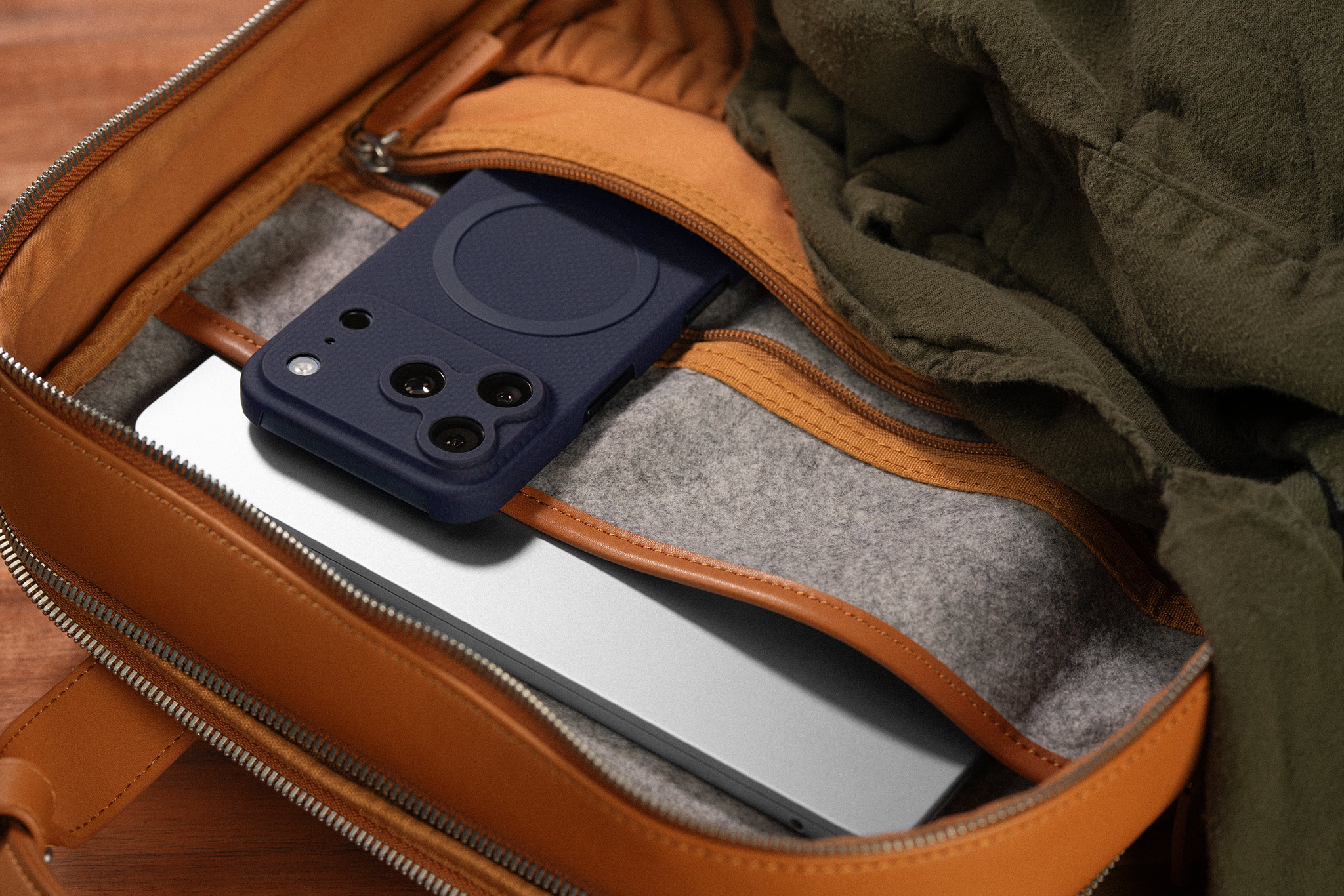 Phone and laptop partially inside a brown bag with a green fabric.