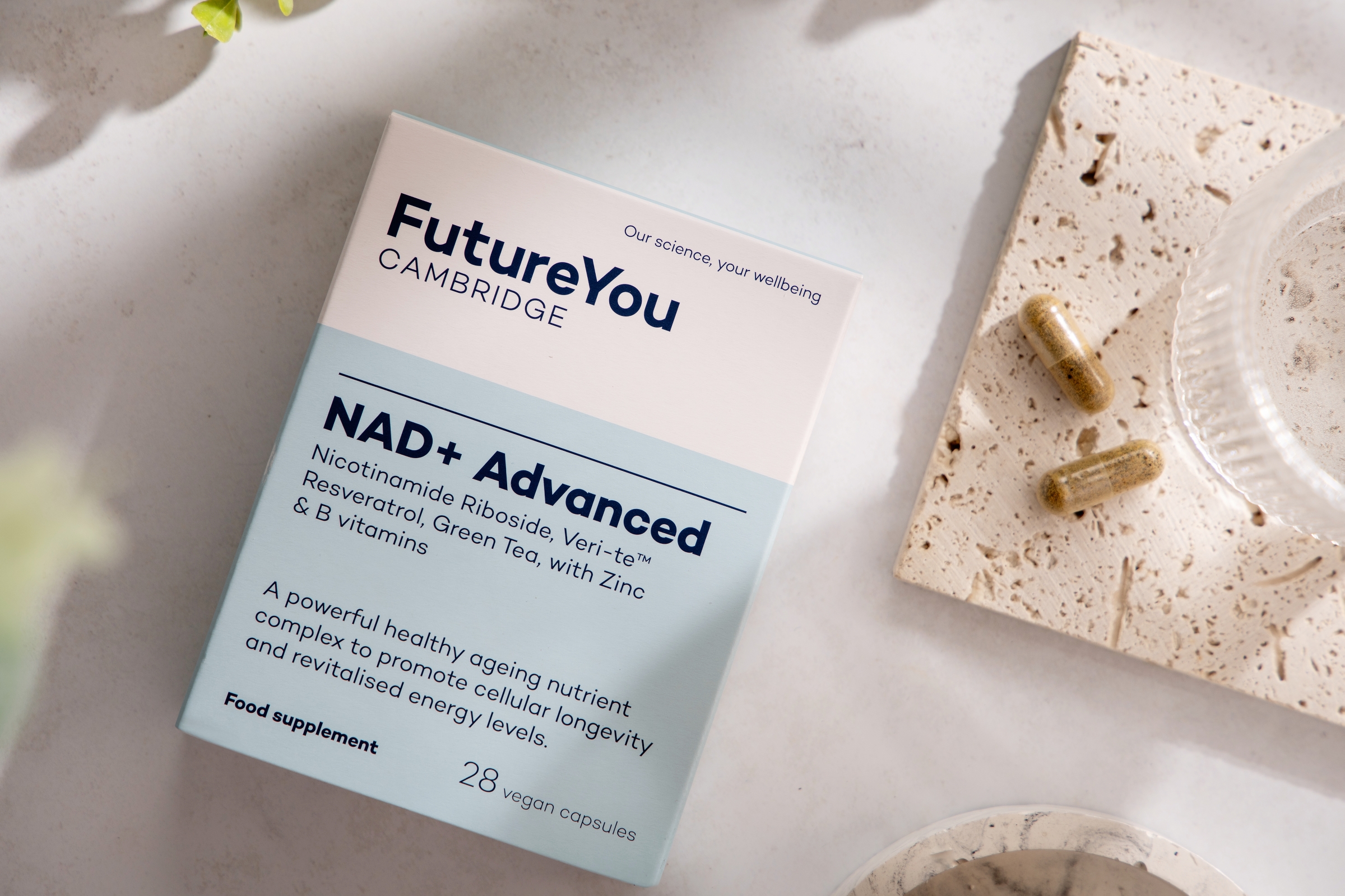 A box of FutureYou NAD+ Advanced supplements next to two capsules on a stone coaster.