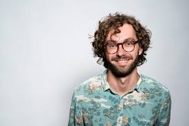 Man with curly hair and glasses wearing a floral shirt, smiling against a plain background.