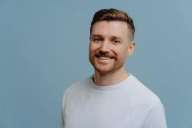 Smiling man in a white shirt against a blue background.