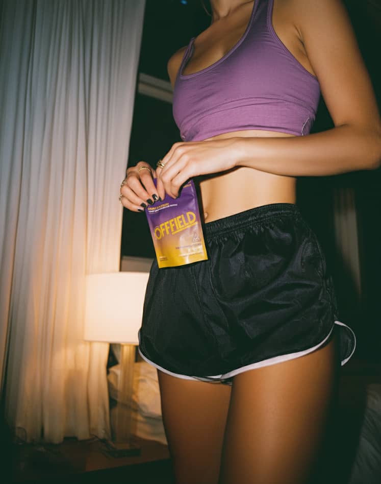 A person in a purple sports bra and black shorts holding a purple and yellow pouch.