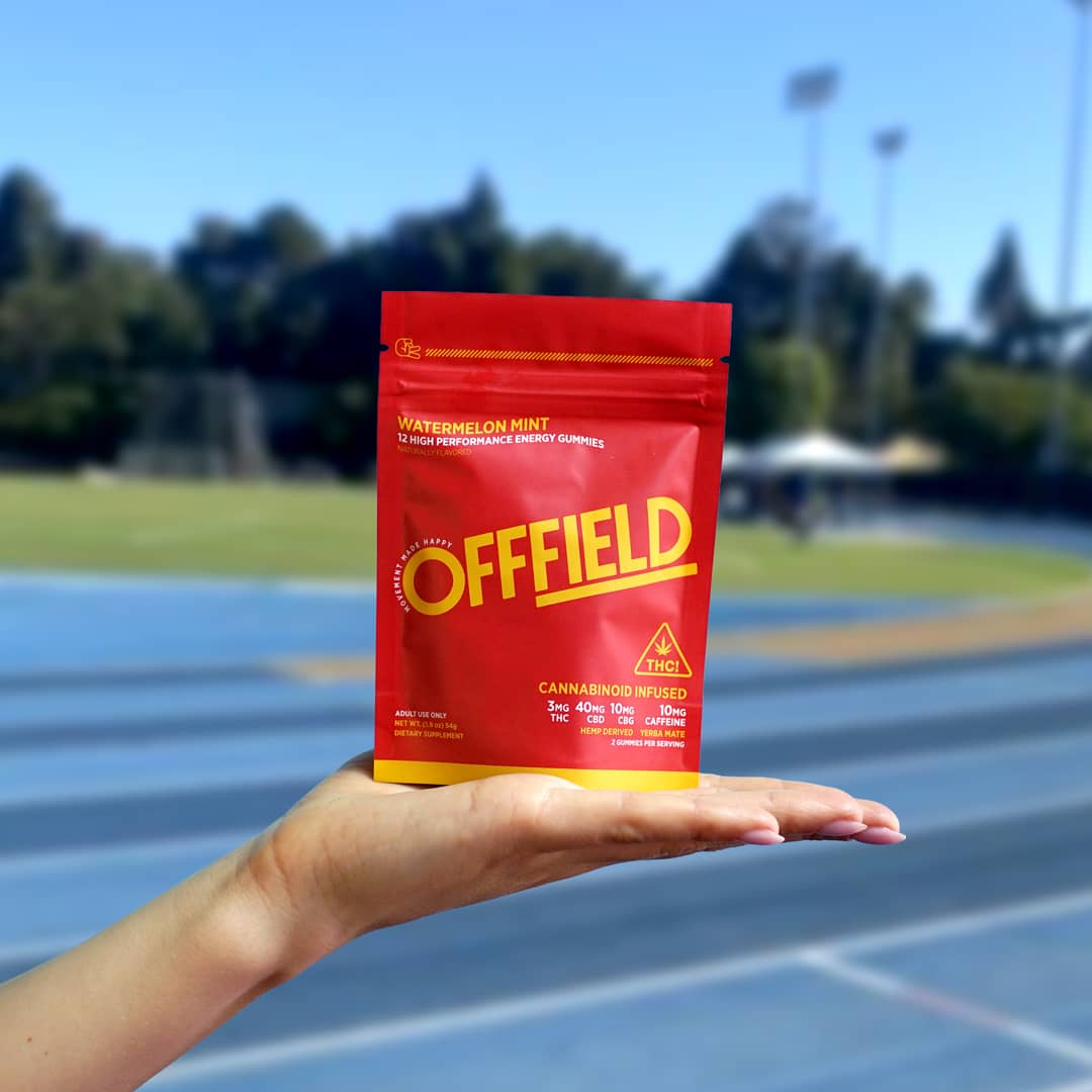 A hand holding a red package labeled 'OFFFIELD' at a track field.