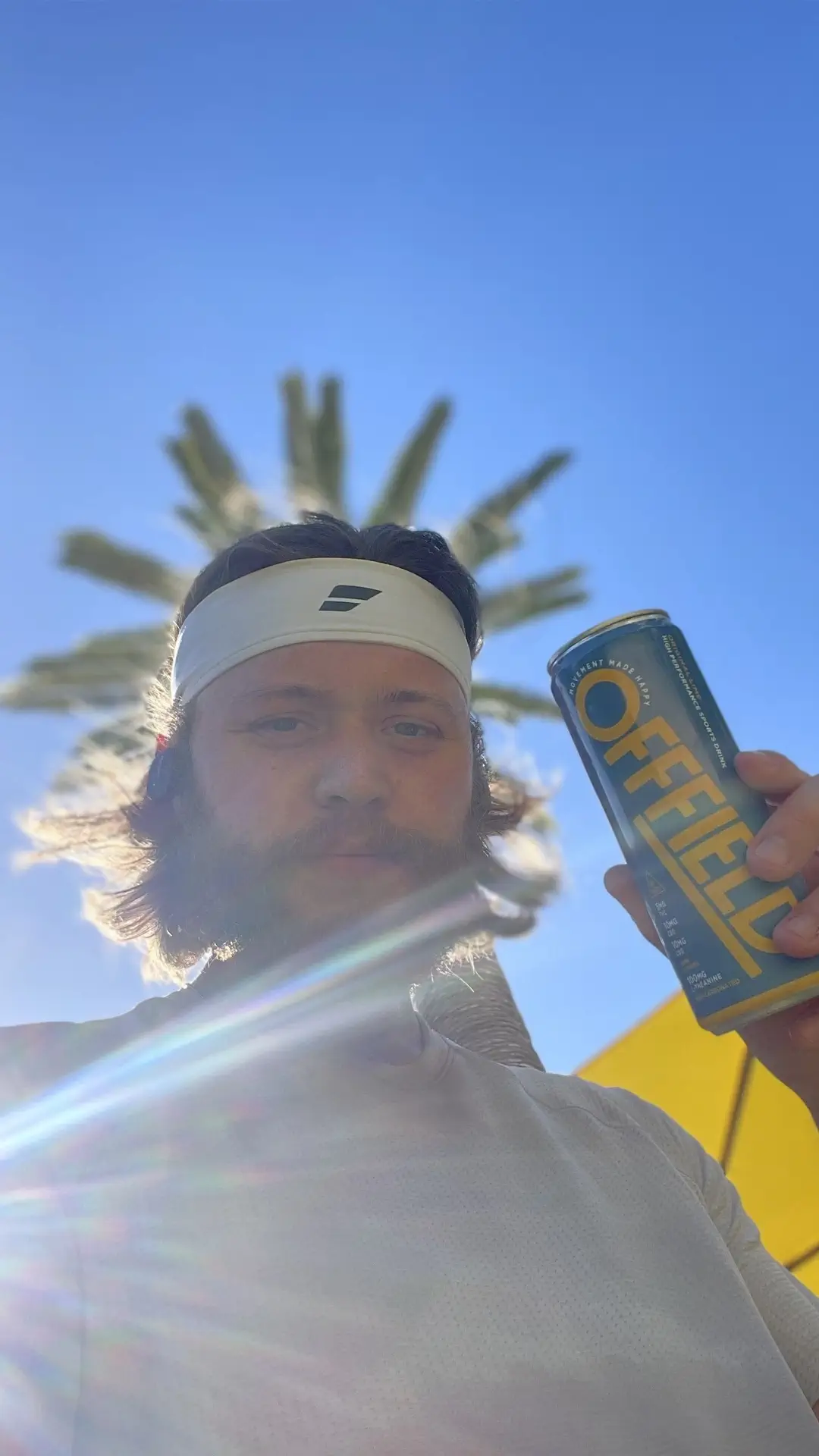 Person outdoors holding an 'OFFFIELD' can with palm tree and blue sky background.