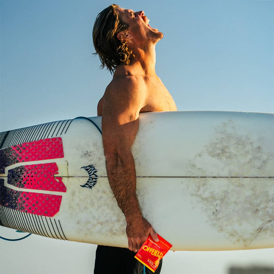 Person holding a surfboard with red grips, looking upwards under a clear blue sky.