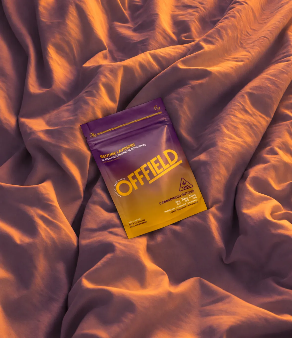 A purple and yellow pouch of Offfield sleep gummies rests on rumpled bedsheets in warm lighting.