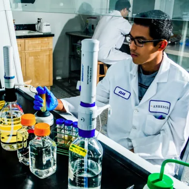 A young man in a lab coat and glasses works with equipment and liquids in a laboratory.