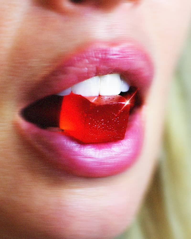 Close-up of lips holding a red gummy candy.