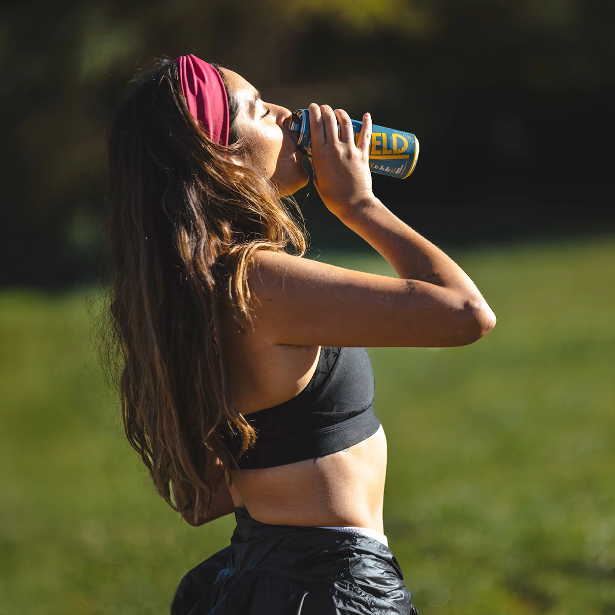 Woman in sportswear drinking from a can outdoors.