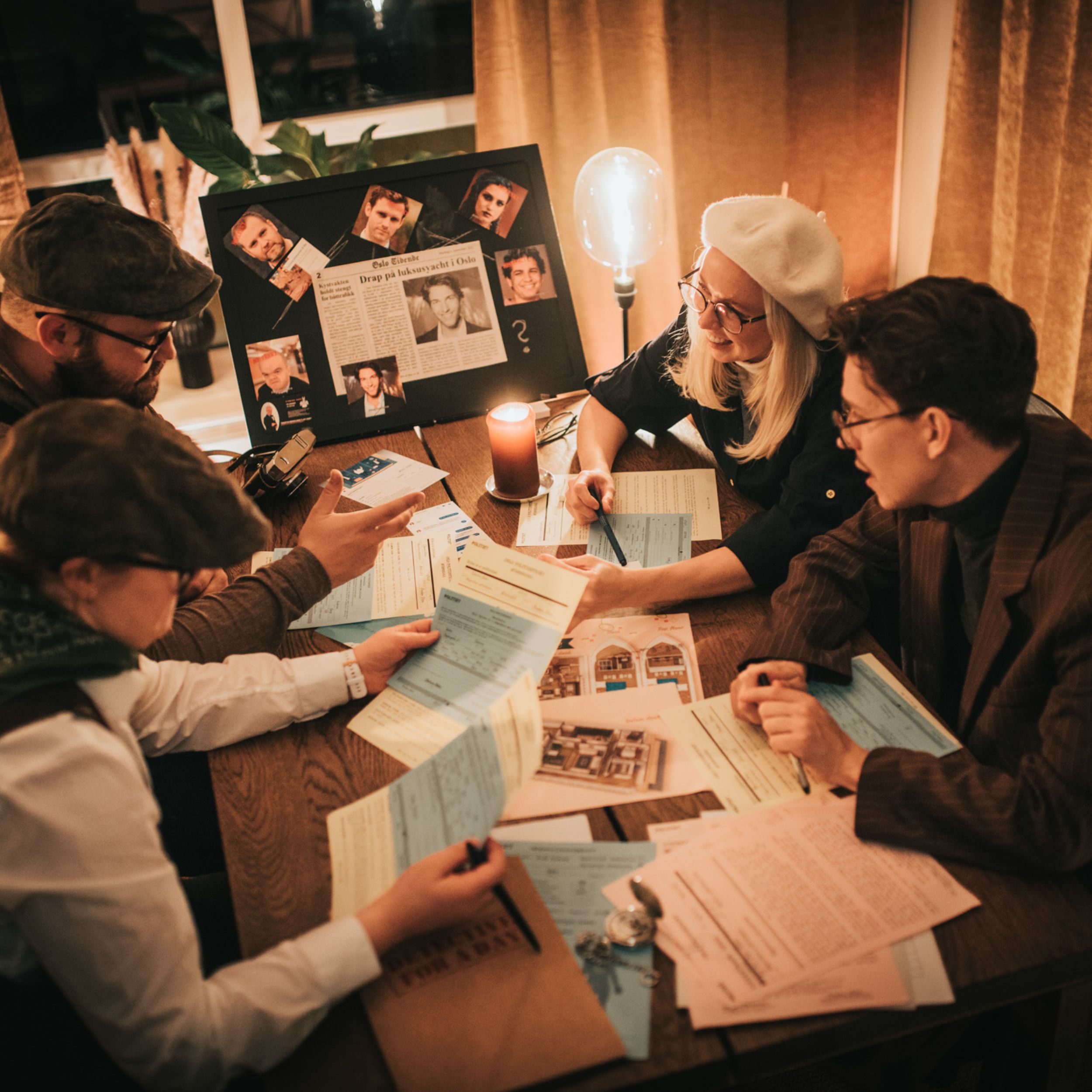 Four people discussing documents around a table with a board of photos and articles.