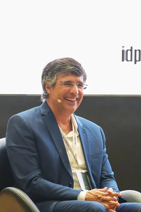 A man with glasses and a blue blazer smiles while wearing a small microphone on his face.