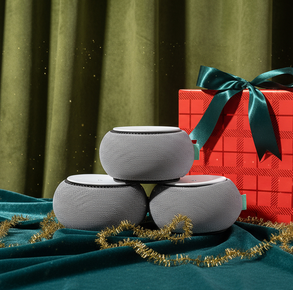 Three gray speakers stacked near a red gift box with green ribbon.