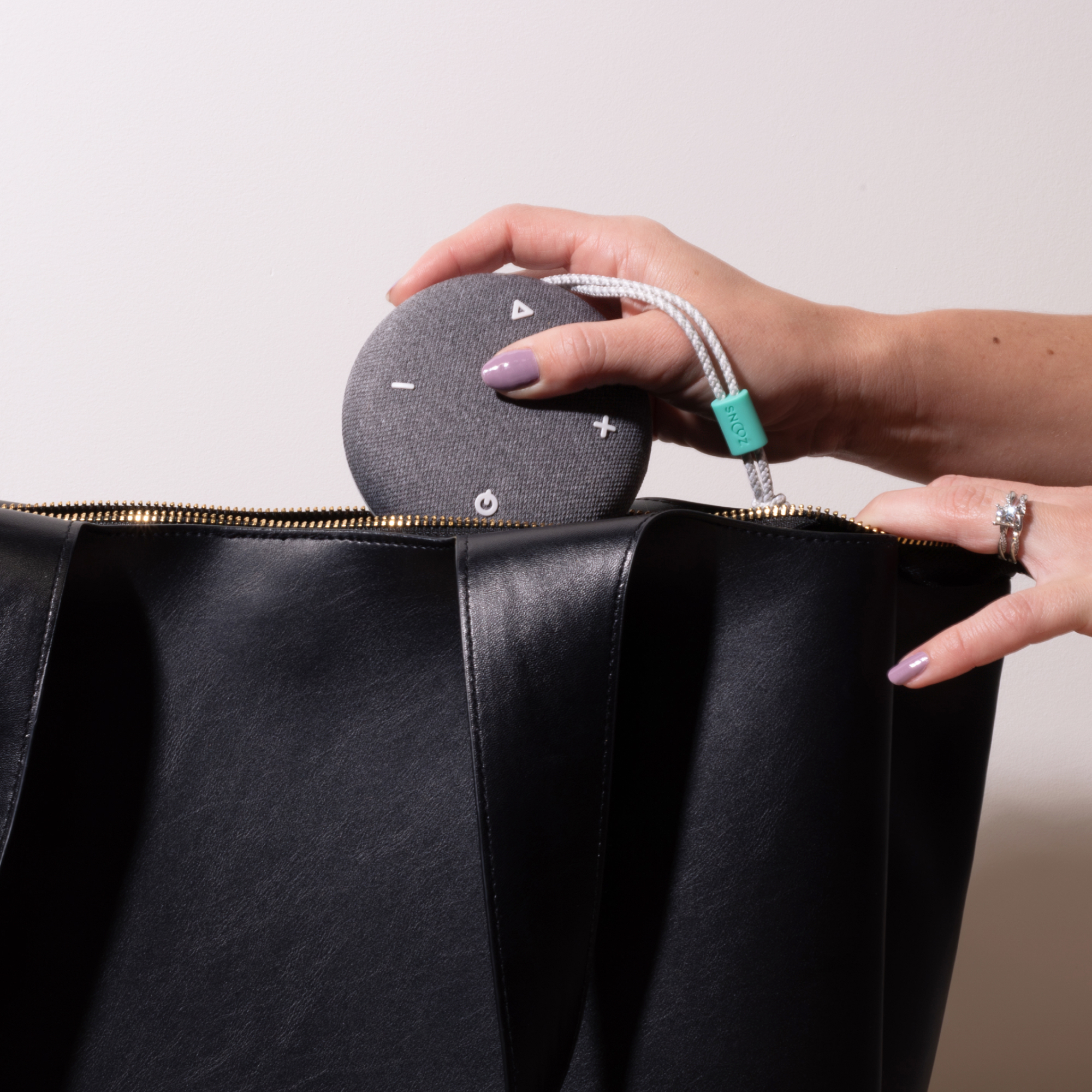 Hand placing a small round speaker into a black leather bag.