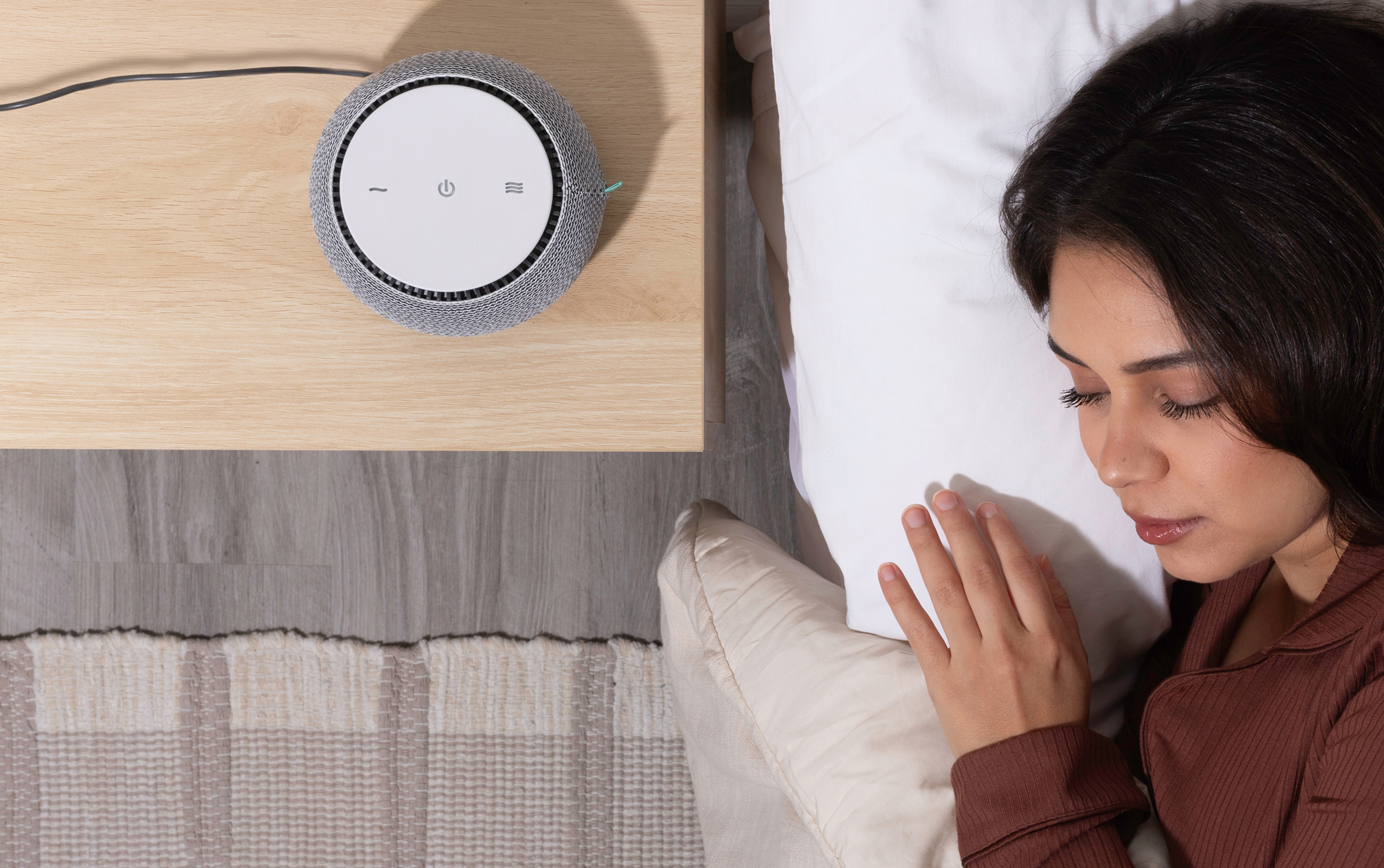 Woman sleeping on a bed beside a circular device on a table.