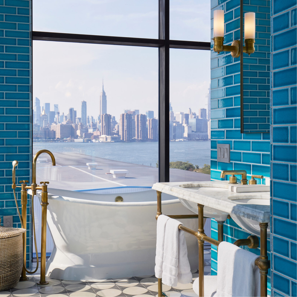 A bathroom with blue tile walls and a large window overlooking a city skyline across the water.