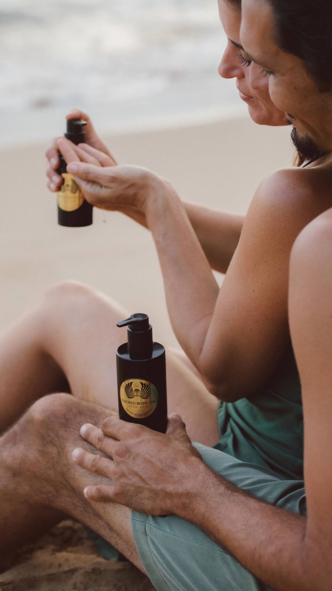 A black pump bottle of Sacred Body Oil with a gold label, resting on a stone surface.