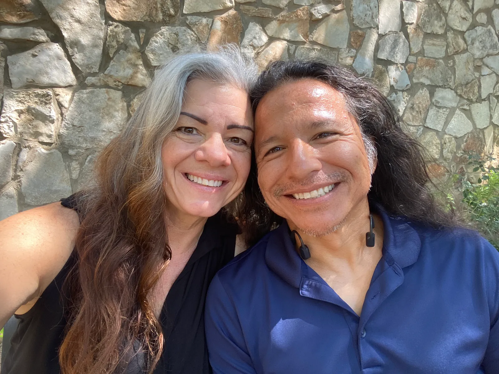 Two people smiling in front of a stone wall.