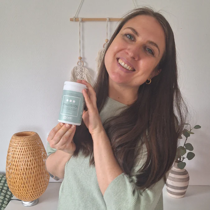 Smiling person holding a container labeled 'XYLOSTITOL' indoors.