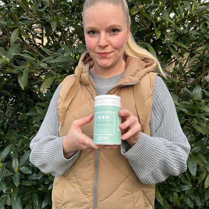 Person holding a container labeled 'Zylositol' in front of green foliage.