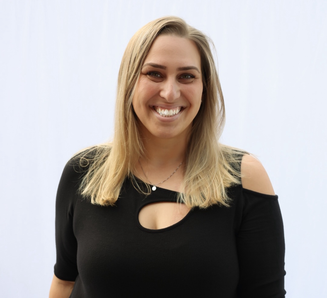 Smiling person with long hair wearing a black top against a white background.