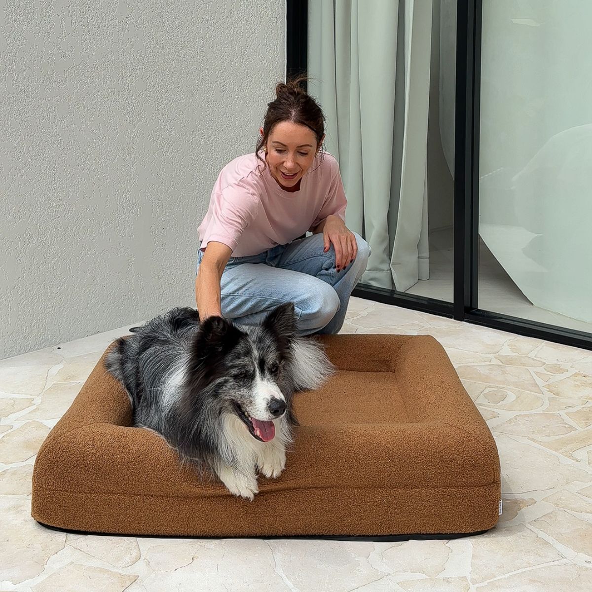 Woman petting a black and white dog on a brown dog bed.