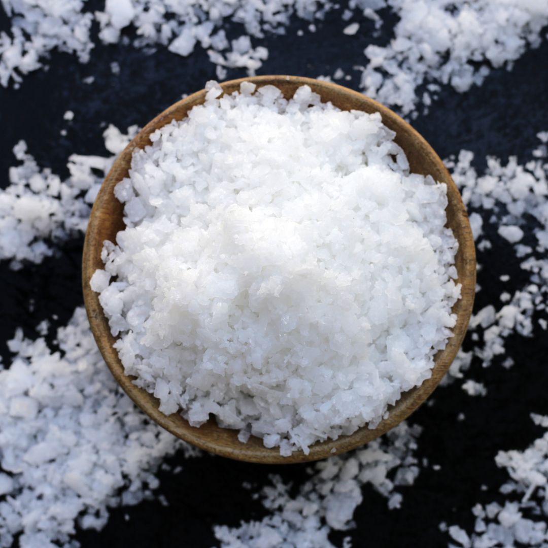 Wooden bowl filled with coarse white salt on a dark surface.