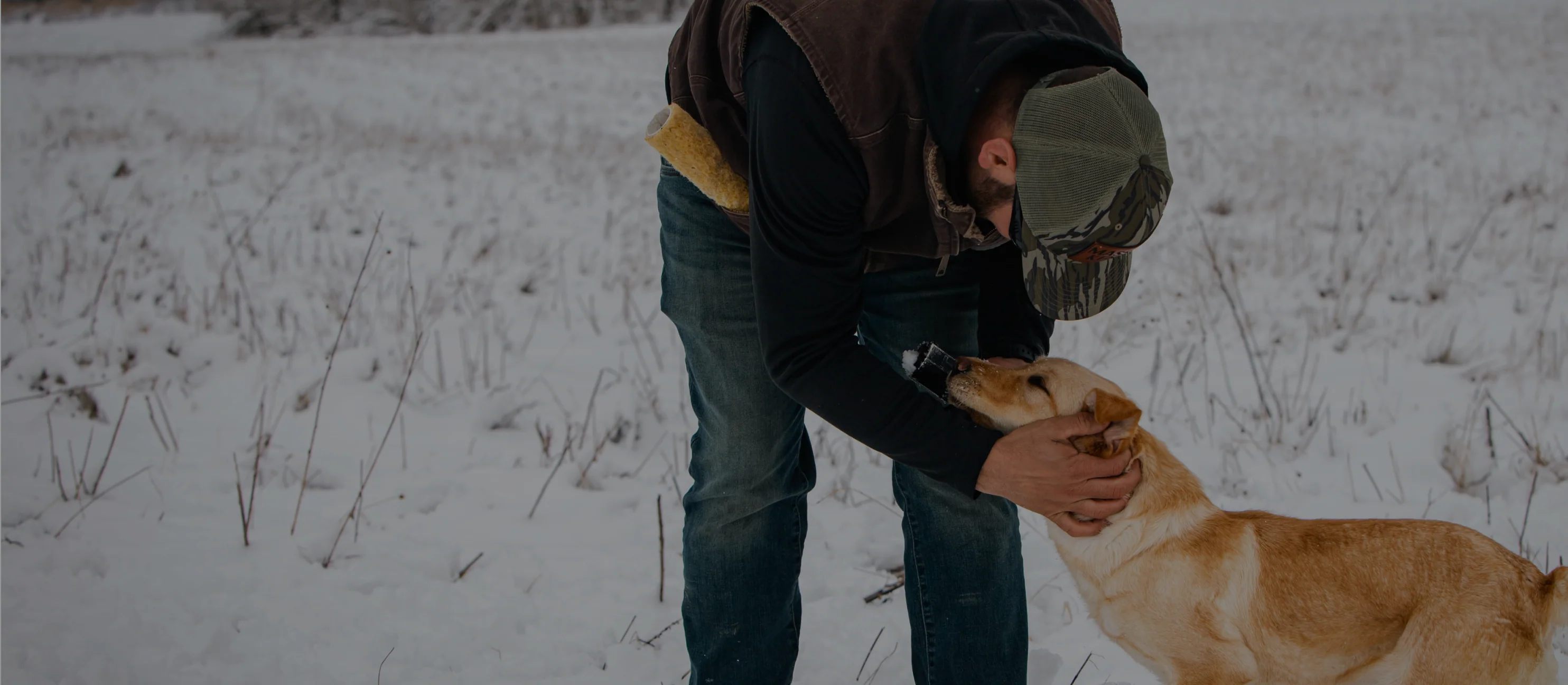 Person in a cap petting a dog in a snowy setting.
