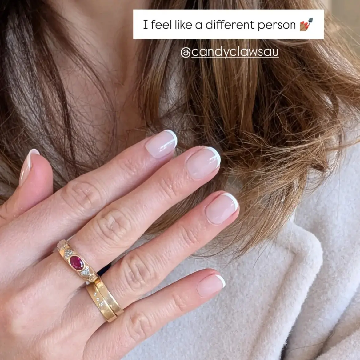 Hand with French manicure and gold rings, touching brown hair.