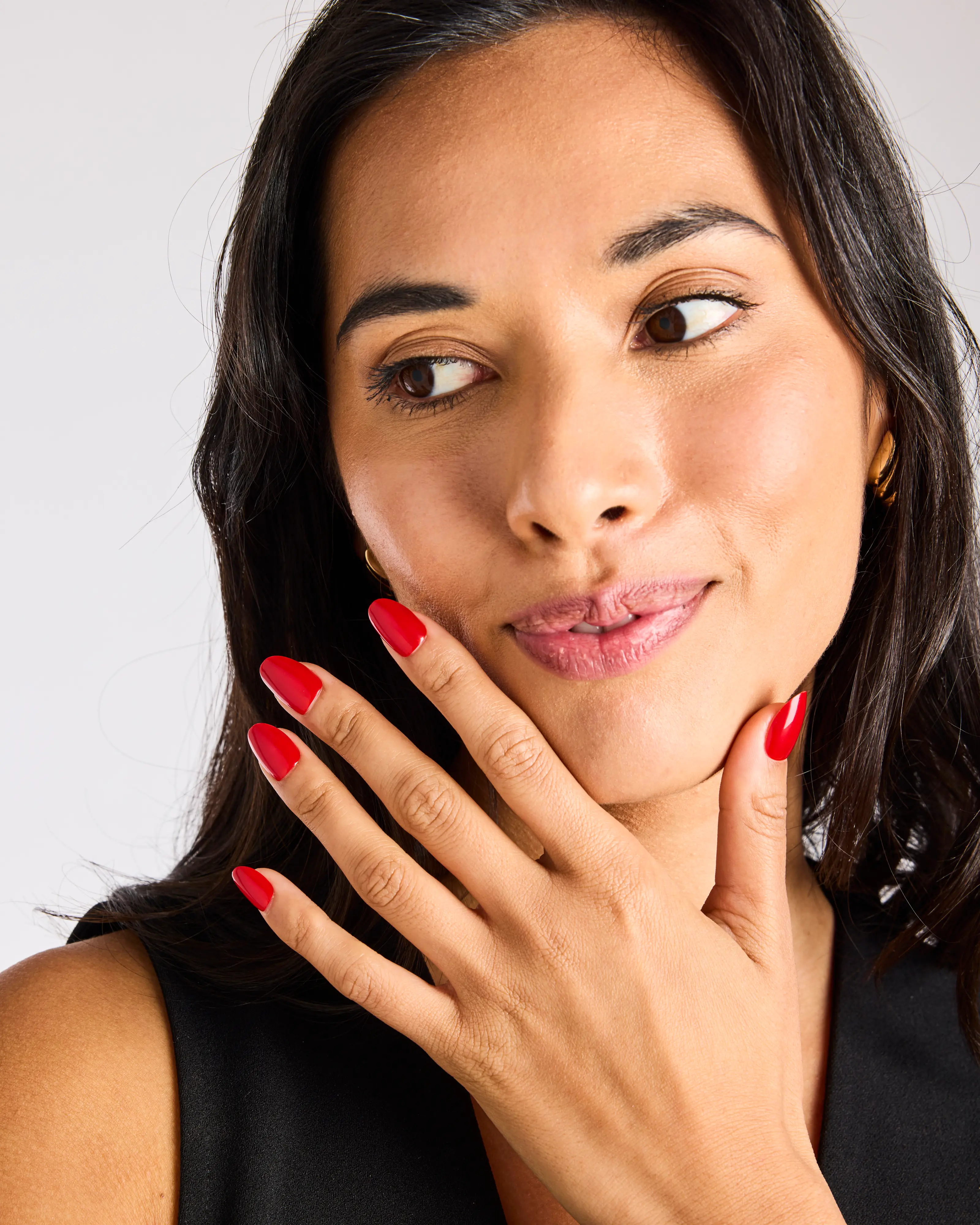 Woman with red nails touching her face, looking to the side.