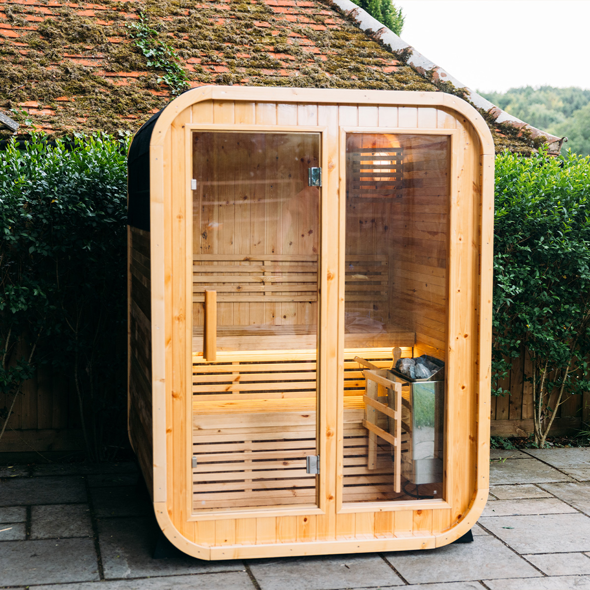 Wooden outdoor sauna with glass door on a patio.